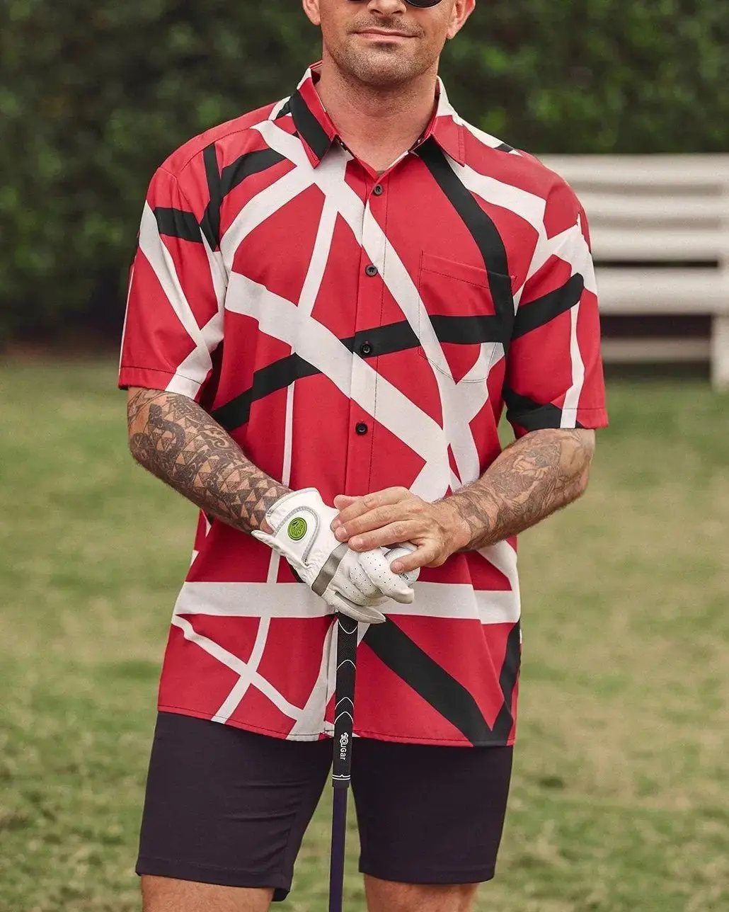 Man in a red and black patterned shirt holding a golf club on a golf course.
